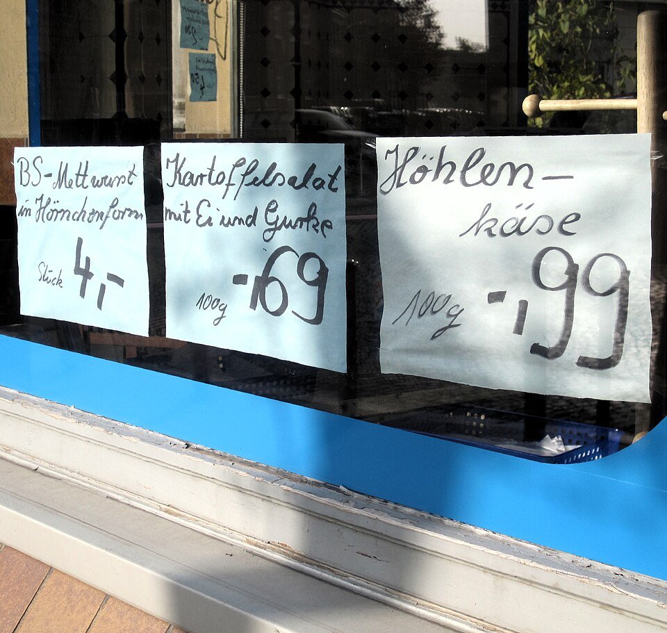 Étiquettes manuscrites dans la vitrine d'une boucherie allemande, affichant des prix à 69 et 99 centimes